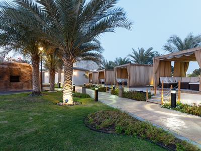 Entspannende Außenanlage mit Palmengärten und überdachten Betten unter blauem Himmel.