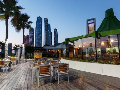 Offener Sitzbereich eines Restaurants mit Blick auf moderne Wolkenkratzer bei Sonnenuntergang.