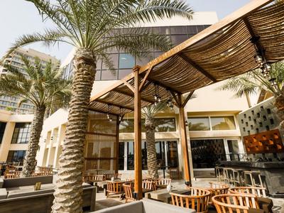 Moderner Außenbereich eines Hotels mit Holzpergola, Palmengarten und Sitzgelegenheiten im Freien.