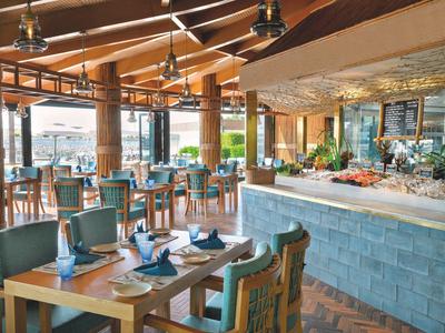 Helles Restaurant mit Holzbalkendecke, grünen Sesseln und Buffet mit frischem Obst.