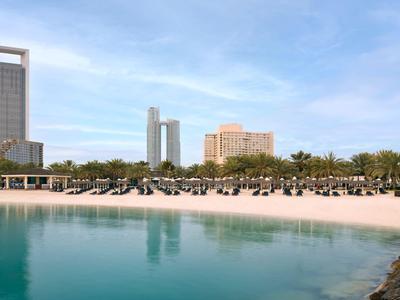 Strand mit vielen Liegestühlen und Hochhäusern im Hintergrund unter blauem Himmel.