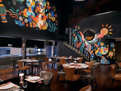 Modernes Restaurant mit bunten Wandgemälden und elegant gedeckten Tischen in einem dunklen Ambiente.