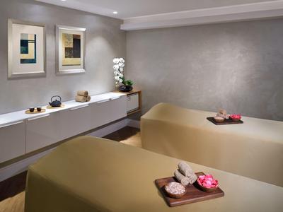 Zwei Massagebetten in einem ruhigen Behandlungsraum mit dekorativen Bildern und Orchideen.