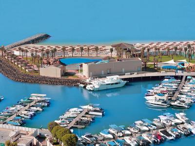 Vogelperspektive auf eine Marina mit Yachten neben einem Hotel und Poolbereich am Meer.