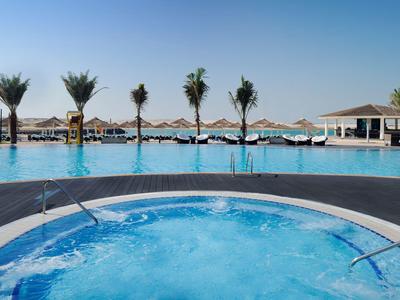 Whirlpool mit sprudelndem Wasser vor einem Pool mit Palmen und Sonnenschirmen.