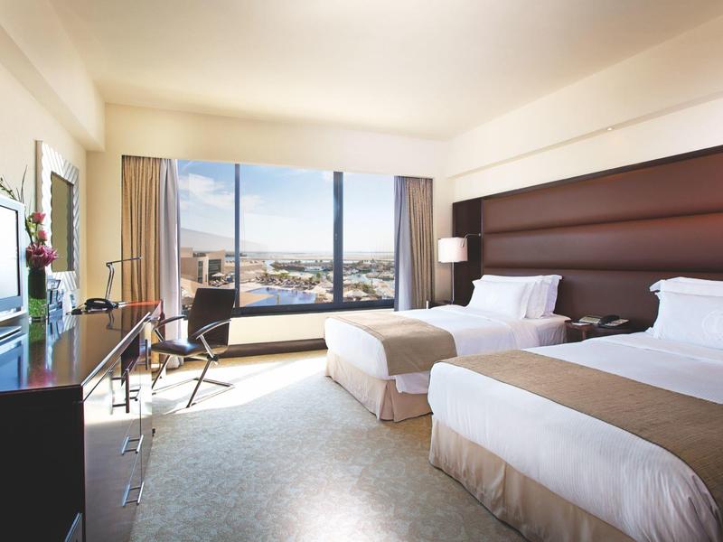 Modernes Hotelzimmer mit zwei Betten und großer Fensterfront mit Stadtblick.