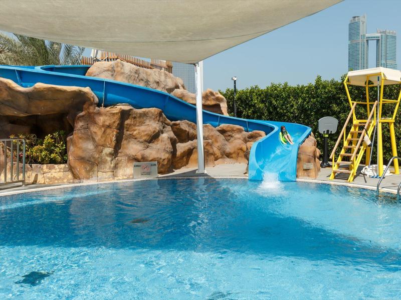 Wasserpark mit Pool, blauer Rutsche und Rettungsschwimmerturm an einem sonnigen Tag