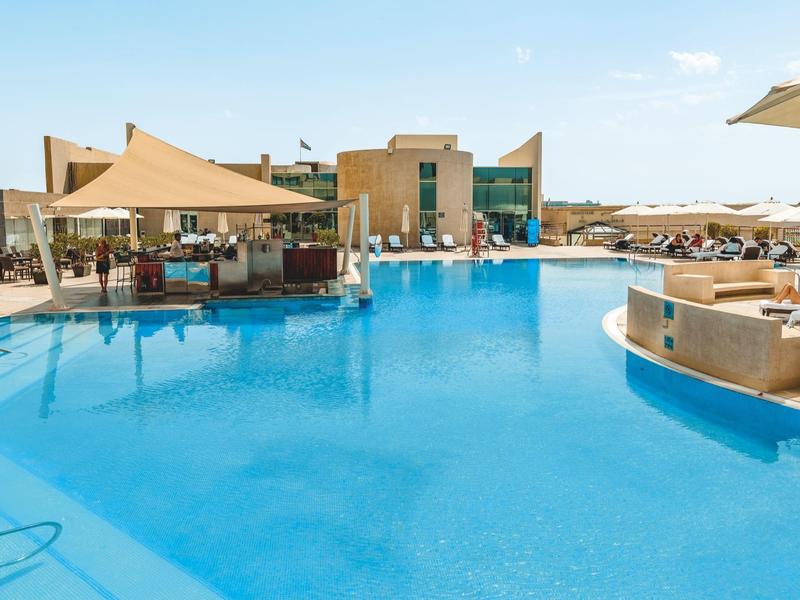 Großer Außenpool mit Sonnensegeln und Liegestühlen in einem Hotelresort.