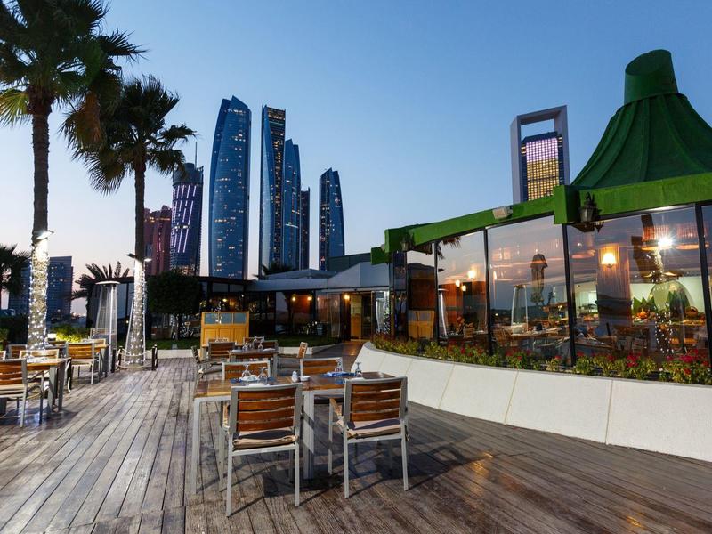 Offener Sitzbereich eines Restaurants mit Blick auf moderne Wolkenkratzer bei Sonnenuntergang.