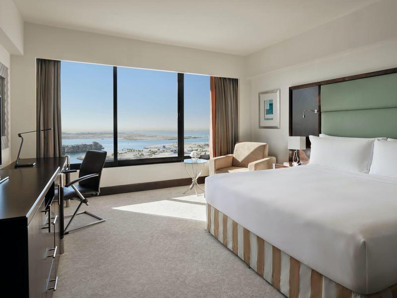 Helles Hotelzimmer mit großem Bett, Sessel, Schreibtisch und weitem Blick auf das Meer.