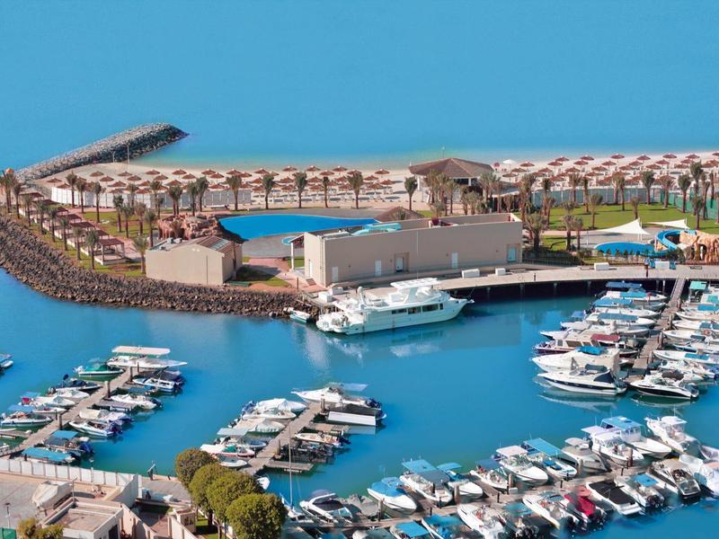 Vogelperspektive auf eine Marina mit Yachten neben einem Hotel und Poolbereich am Meer.