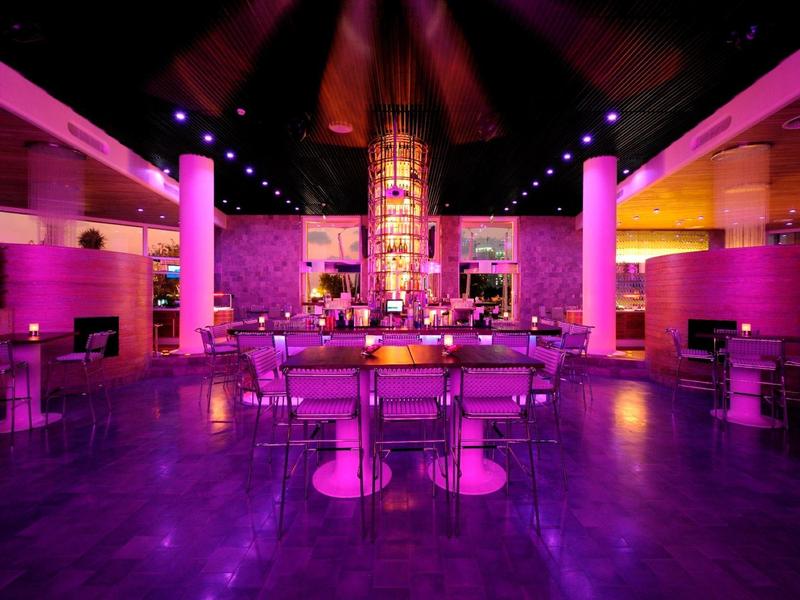 Moderner Hotelbarbereich mit lila Beleuchtung und Sitzgelegenheiten in futuristischem Design.