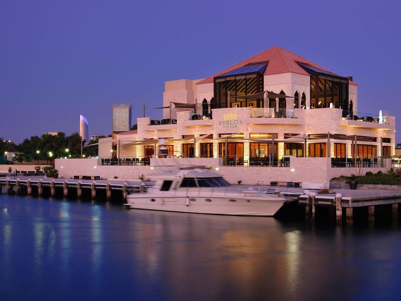 Modernes Hotel mit Yacht und beleuchtetem Pier bei Dämmerung am Wasser