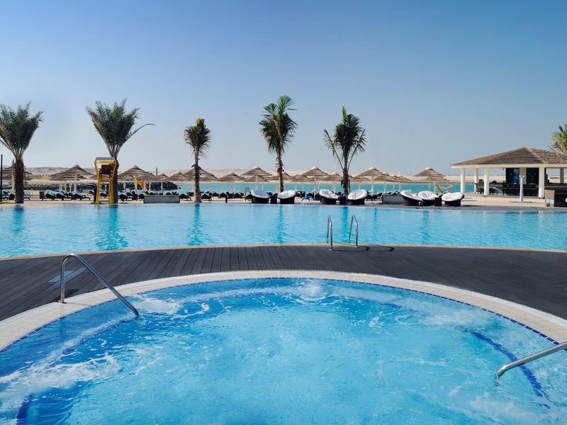 Whirlpool mit sprudelndem Wasser vor einem Pool mit Palmen und Sonnenschirmen.