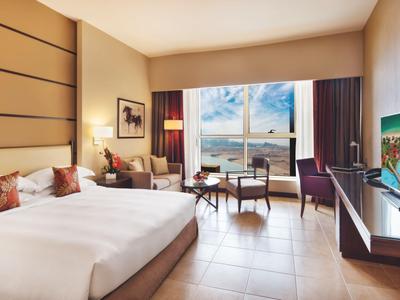 Modernes Hotelzimmer mit Doppelbett, Sessel, Schreibtisch und Blick auf das Meer durch große Fenster.