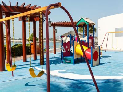 Moderner Kinderspielplatz mit Schaukel, Rutsche und Klettergerüst auf blauem Gummiboden.