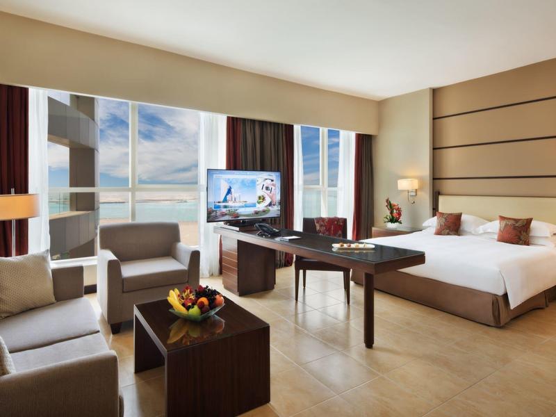 Modernes Hotelzimmer mit Doppelbett, Sofa, Schreibtisch, Fernseher und großem Fenster mit Stadtblick.