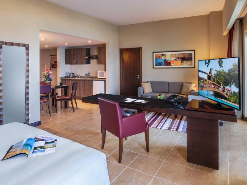 Modern eingerichtetes Wohn- und Schlafzimmer mit Fernseher, Schreibtisch, Essbereich und großer Glasfront.