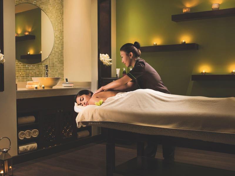 Entspannter Massageraum mit warmem Licht, Kerzen und einer Frau, die auf einem Tisch massiert wird.