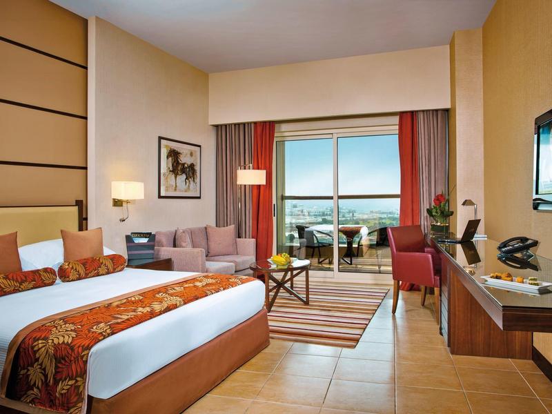 Modernes Hotelzimmer mit großem Bett, Sofa, Schreibtisch und Balkon mit Meeresblick.