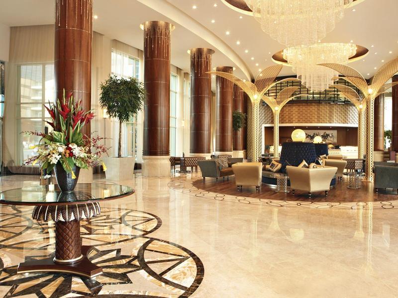 Große Hotellobby mit glänzendem Marmorfußboden, Säulen, luxuriösem Kronleuchter und Sitzgruppen.