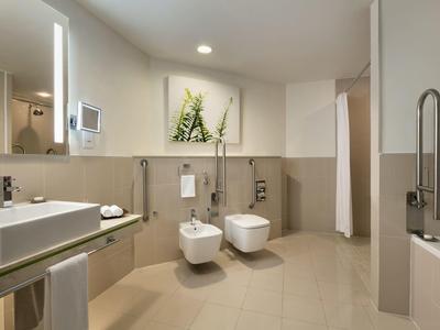 Moderner Badezimmerschr<R: mit weißen Armaturen, beige Fliesen und grünem Pflanzenbild an der Wand.