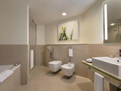 Helles modernes Bad mit Wand-WC, Bidet, Waschbecken, Spiegel und Kunstwerk an der Wand.