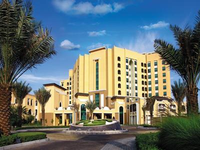 Großes gelbes Hotelgebäude mit mehreren Stockwerken, Palmen und blauem Himmel im Hintergrund.