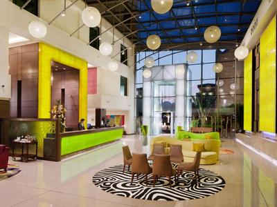 Moderner Hotellobby mit grünen Akzenten, runden Sesseln, Glasdach und hellem, offenem Raum.