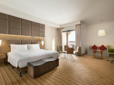 Geräumiges Hotelzimmer mit großem Bett, Holzfußboden, Sofa und Schreibtisch neben Balkonfenster.