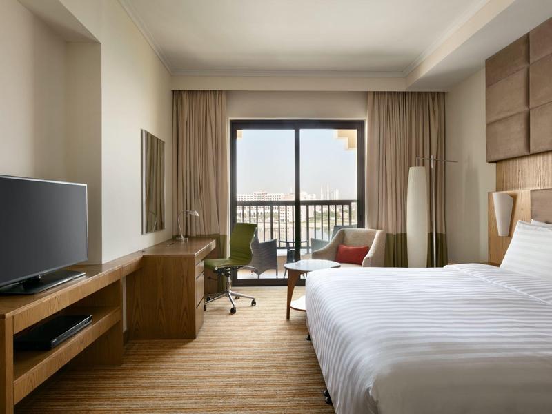 Modernes Hotelzimmer mit großem Bett, Schreibtisch, Fernseher und Balkon mit Cityblick.