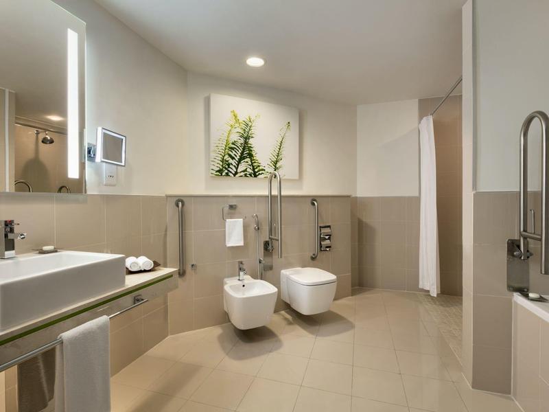 Moderner Badezimmerschr<R: mit weißen Armaturen, beige Fliesen und grünem Pflanzenbild an der Wand.