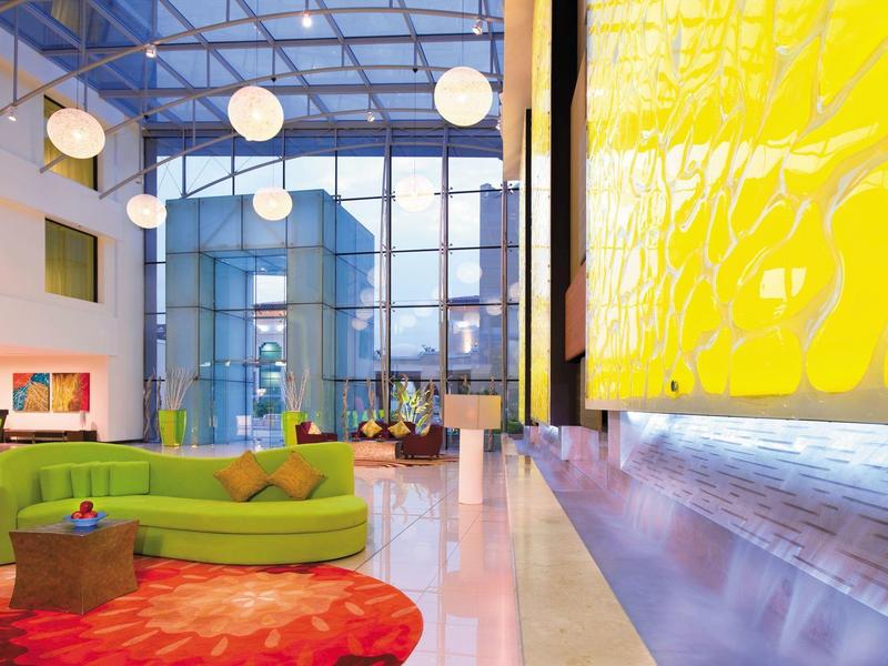 Helle, moderne Lobby mit großen Glasfenstern, gelber Wand, grüner Couch und rotem Teppich.