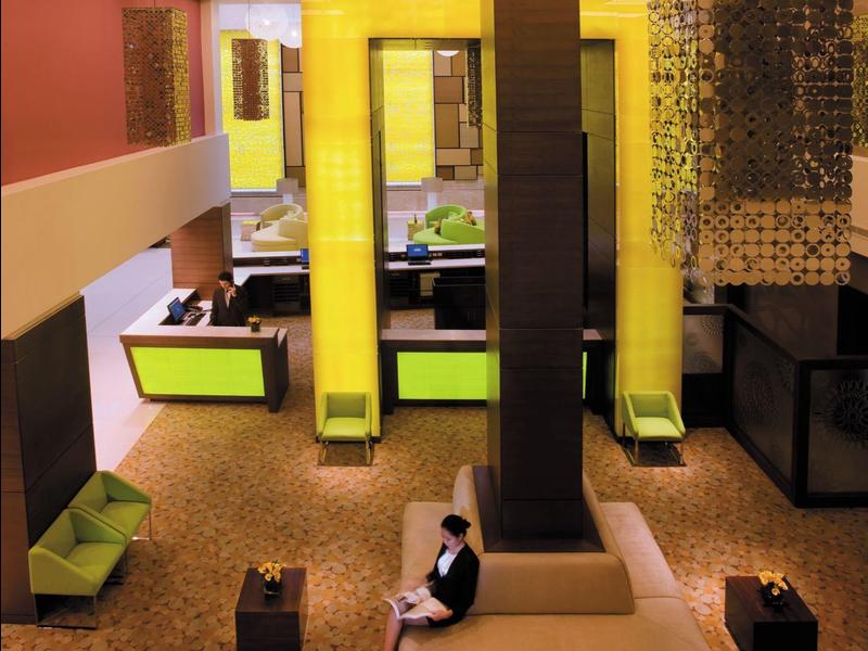 Moderne Lounge mit gelborangen Wänden, grünen Sitzpolstern und geometrischen Leuchten.