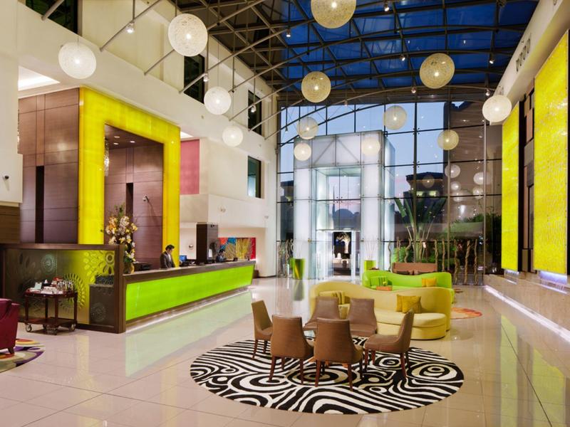 Moderner Hotellobby mit grünen Akzenten, runden Sesseln, Glasdach und hellem, offenem Raum.