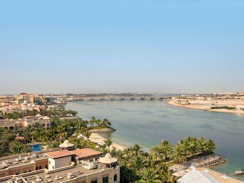 Breiter Fluss mit grünen Ufern, Brücke im Hintergrund und blauem Himmel darüber.