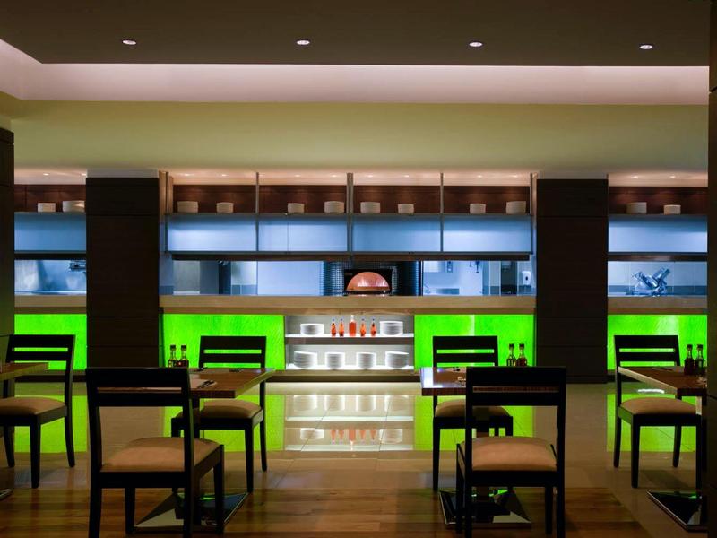 Moderne Bar mit beleuchteten Regalen, Holzmöbeln und grünem Akzentlicht.