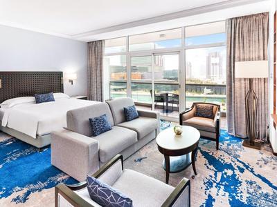 Modern eingerichtetes Hotelzimmer mit Sofa, Bett, Sesseln und großem Balkon mit Meerblick.