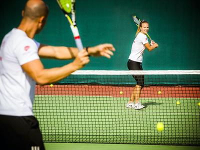 Zwei Personen spielen Tennis auf einem Außenplatz bei Sonnenlicht.