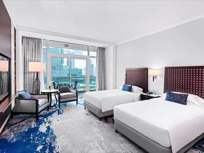 Modernes Hotelzimmer mit zwei Einzelbetten, Sitzbereich und Balkon mit Stadtblick.