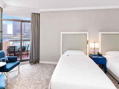 Modernes Hotelzimmer mit zwei Einzelbetten, blauen Sesseln und Balkon mit Meerblick.