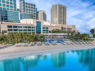 Luxuriöses Strandresort mit Pool, Palmen und modernen Hochhäusern im Hintergrund.