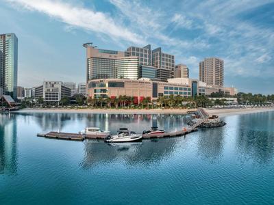 Moderner Hafen mit Booten vor einer Stadtkulisse und Hochhäusern bei klarem Himmel.