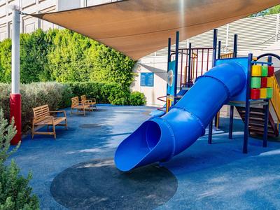 Kinderspielplatz mit blauem Röhrenrutsche und Sitzbank im Schatten eines Sonnensegels
