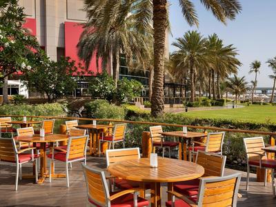 Außenbereich eines Restaurants mit Holztischen und Stühlen unter Palmen im Sonnenschein.