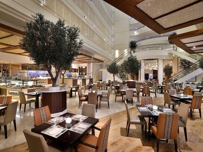 Großer Restaurantbereich mit Tischen, Stühlen und Bäumen in luxuriösem Innenraum.