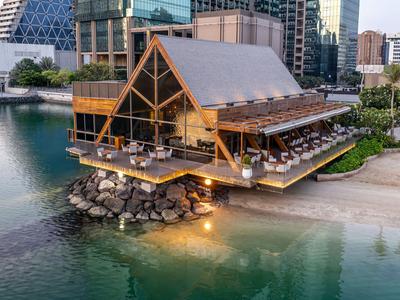 Modernes Restaurant auf Stelzen über Wasser mit Außenbereich und Stadtgebäuden im Hintergrund