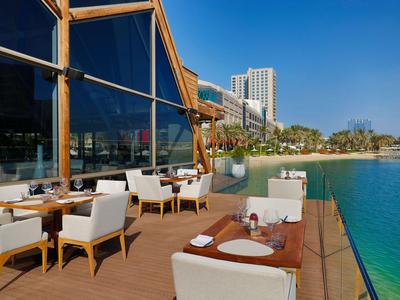 Terrasse eines Hotels mit weißen Stühlen und Tischen am Wasser mit Blick auf die Stadt.