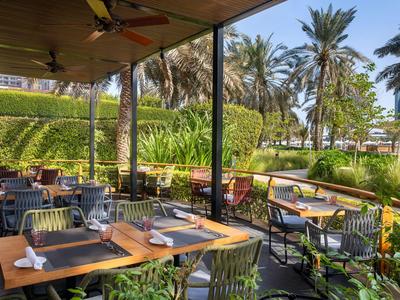 Außenrestaurant mit gedeckten Tischen, Stühlen und Palmen im Hintergrund bei sonnigem Wetter.