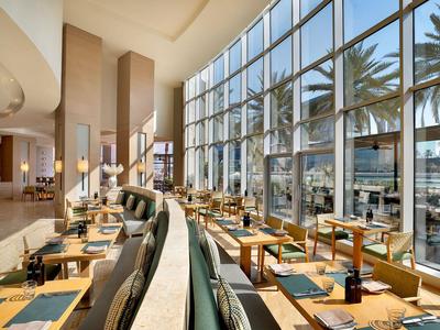 Helles Restaurant mit großen Bodentiefen Fenstern und Blick auf Palmen und Meer